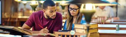 Two students study together at a table with books