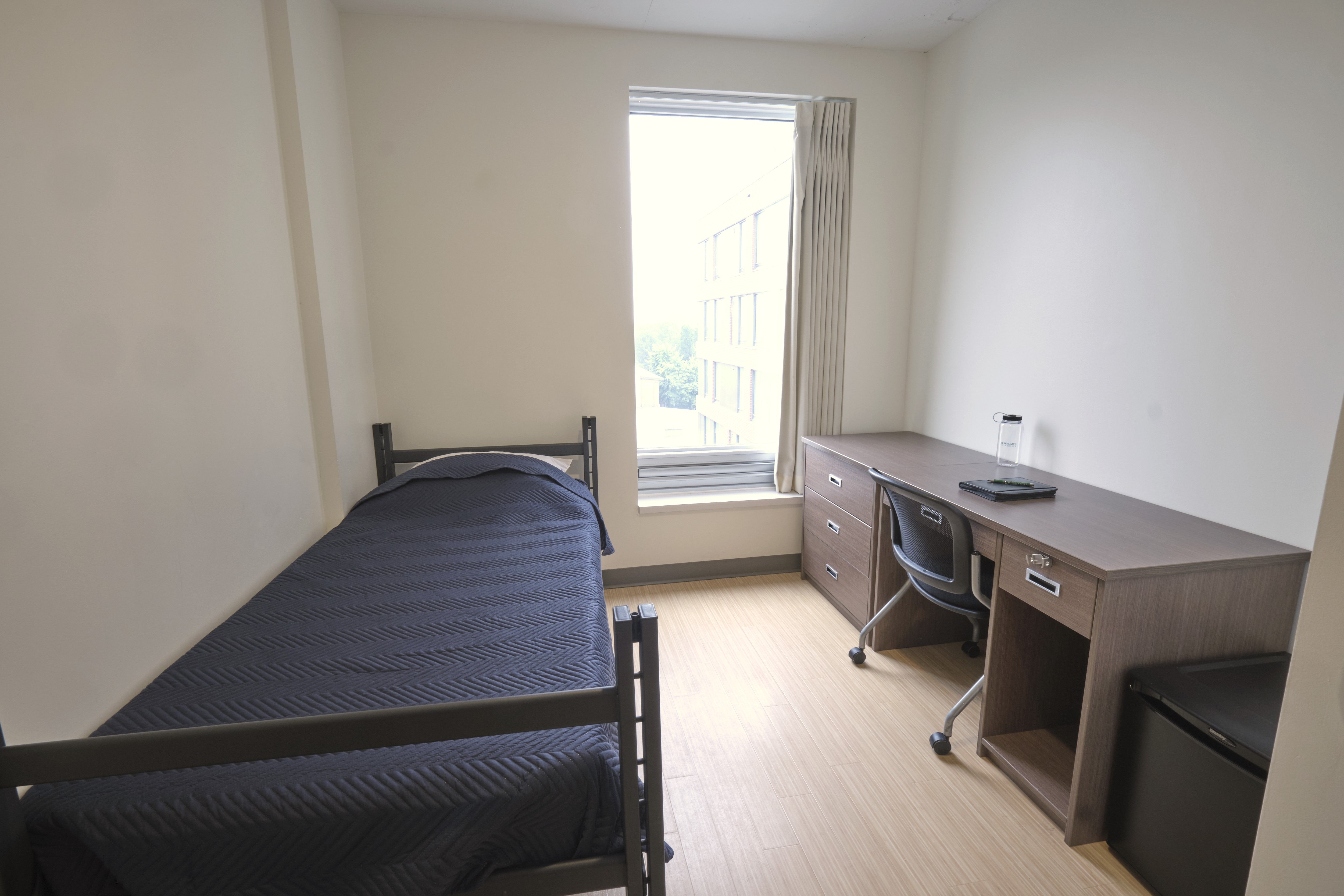 Single residence room with bed, desk, and mini fridge