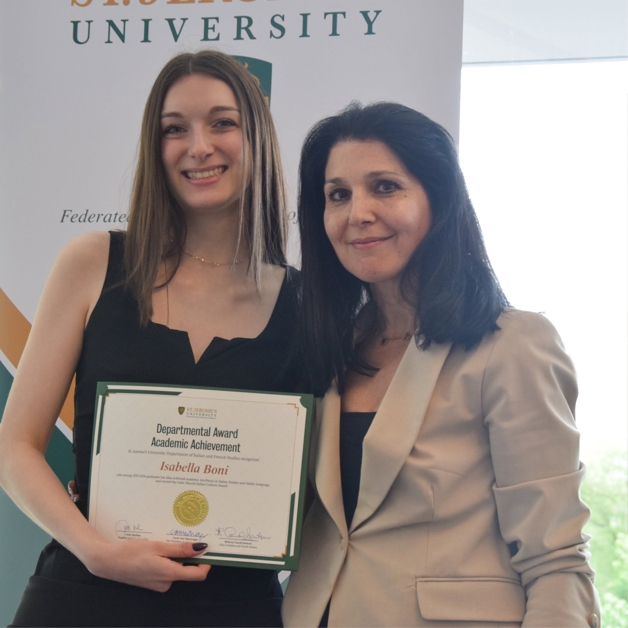 Isabella Boni and Roberta Cauchi-Santoro stand in front of an SJU banner holding the departmental award certificate