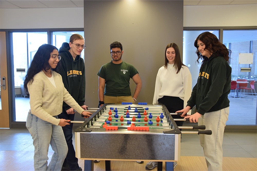 Five students play table hockey in the Siegfried and Ryan Hall common lounge games room