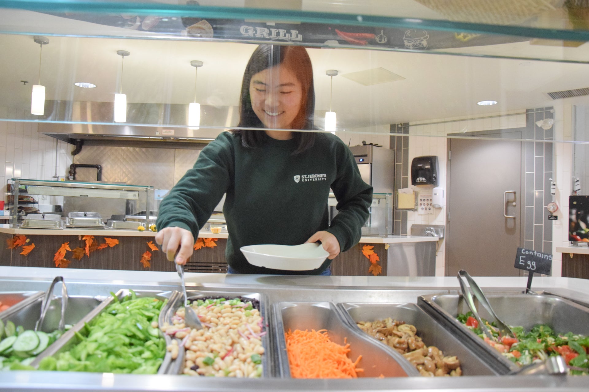 A student filling their plate with vegetables and pastas from the salad bar in the Doug Letson Community Center