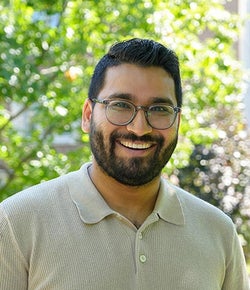 Armaan Dattani portrait, smiling in a white t-shirt in front of trees