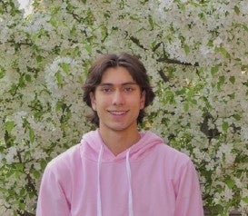 Asher Scaini smiles in front of a white flowering bush