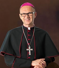 Bishop Dabrowski stands in front of a dark background in his vestiments