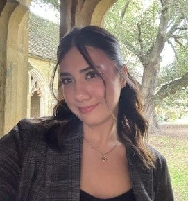 Julia Cockburn smiles in front of a stone arch with trees in the background.