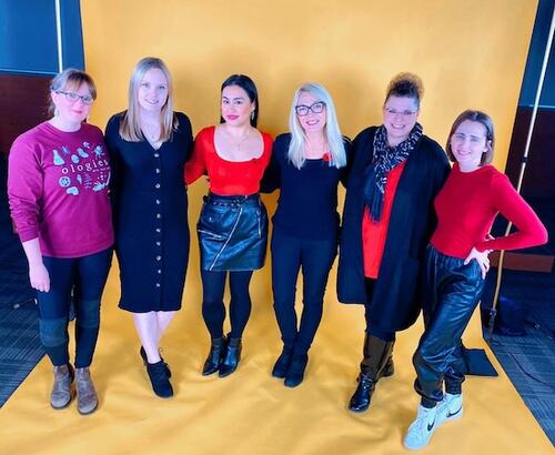 The UWSA Operations Team all wearing red and black, standing in front of a bright yellow photography backdrop.