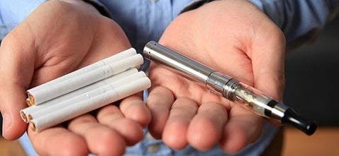 Man holding cigarettes in one hand and an e-cigarette in the other