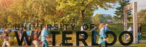 Students walking past UWaterloo sign in fall