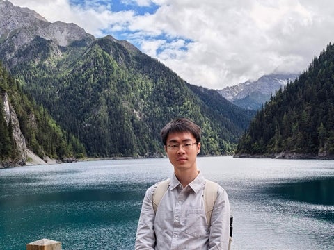 Pingchu Zhang standing in front of a mountain lake. 