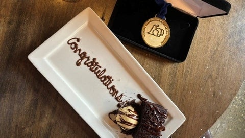 Congratulations written on a plate with cake, posed next to the Eckler medal