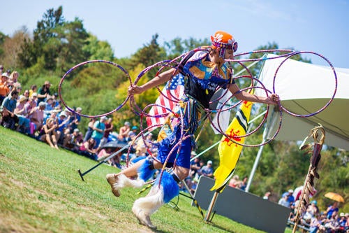 Hoop dancer in brightly coloured regalia with audience in background
