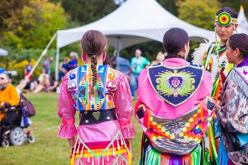 Indigenous dancers wearing brightly colored regalia get ready to perform