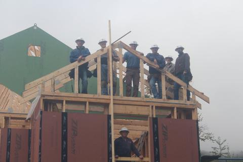 members of a Habitat home build stand among the trusses of a project
