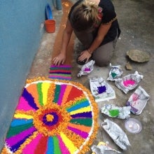 Courtney crouching as she creates colorful rangoli for festival