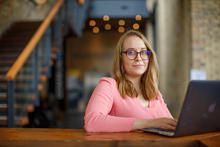 Rachel Thompson sits at a desk with a laptop, staircase in the background