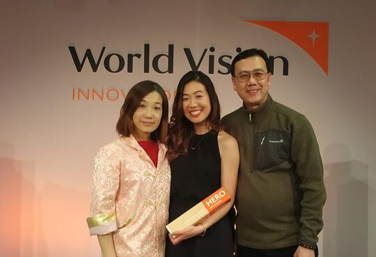 Cherie and her parents pose with the award in front of a World Vision logo
