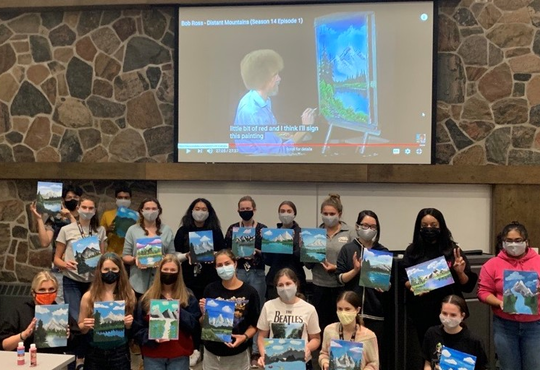 students pose in Alumni Hall with their Bob Ross inspired paintings