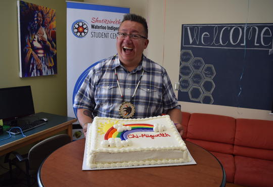 Shawn Johnston flashes a big smile while standing behind a cake that reads chi-miigwetch