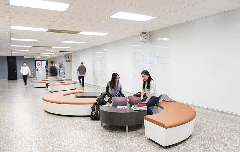 Two students sit on round bench in the Math and Computer building.