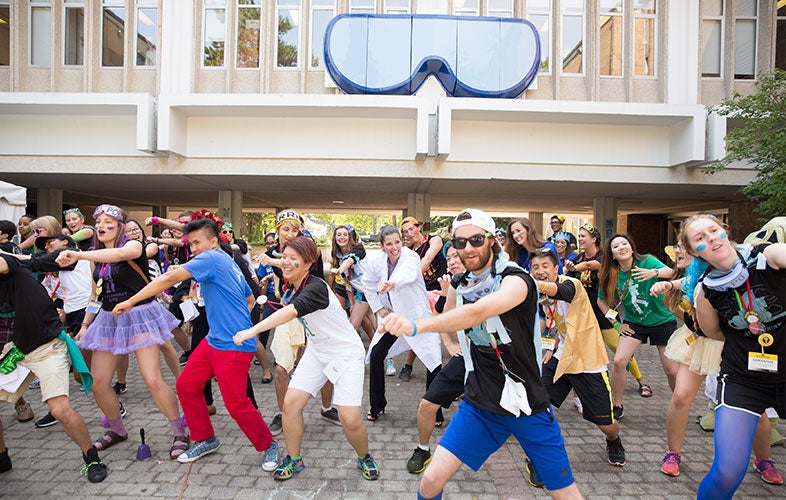 Students dance in a group under science goggles sculpture.