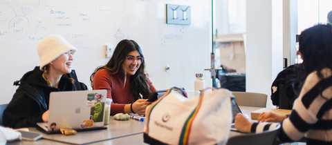 Three students laughing while working on a project in a project room.