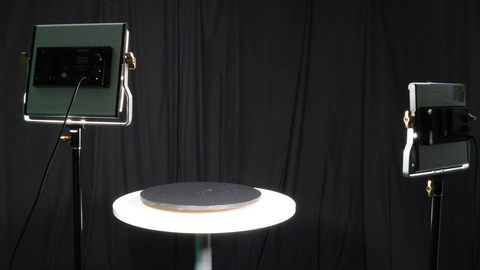 Two lights are on and pointed at a table with a black curtain background