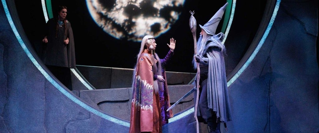 A scene from The Hobbit play. Two actors talk to each other, and one actor watches from the background.