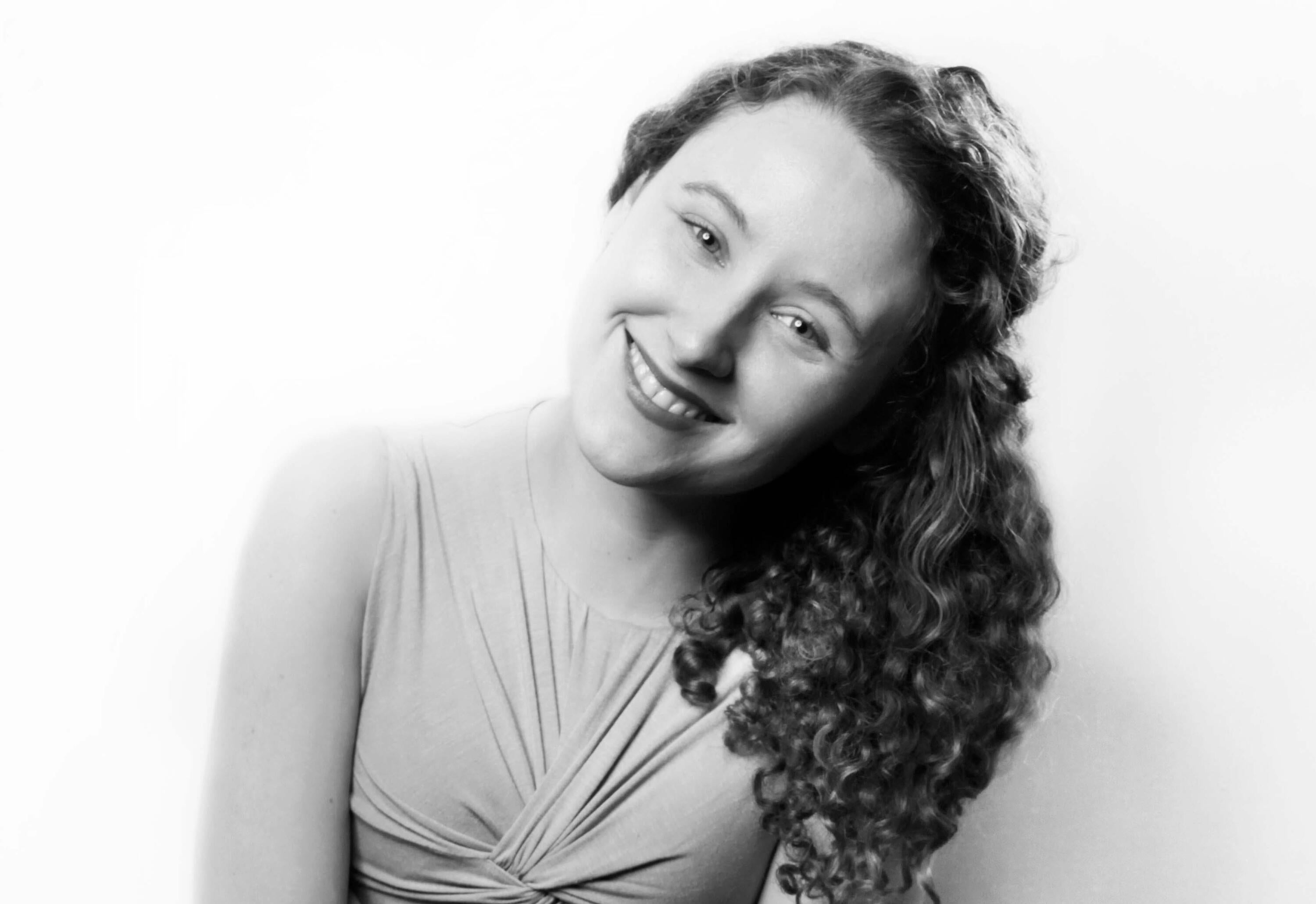 A black and white photograph of a smiling woman with curly hair