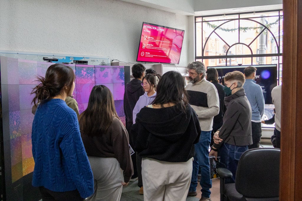 People gathered to look at student projects in front of display wall