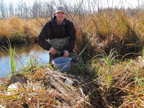 A person collecting a biomonitoring sample from a stream