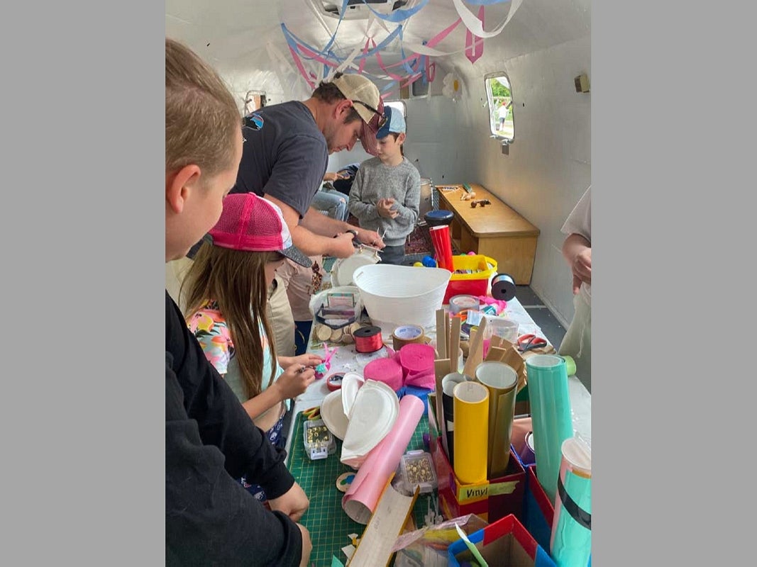 Adult and children gather around a table of craft supplies inside a vintage airstream trailer. 