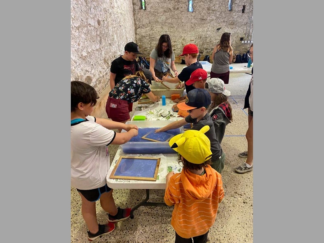 In an old stone building, a group of children gather around table cleaning screens for paper-making.