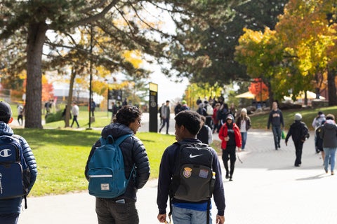 A group of students walking through campus on a sunny, Fall day.