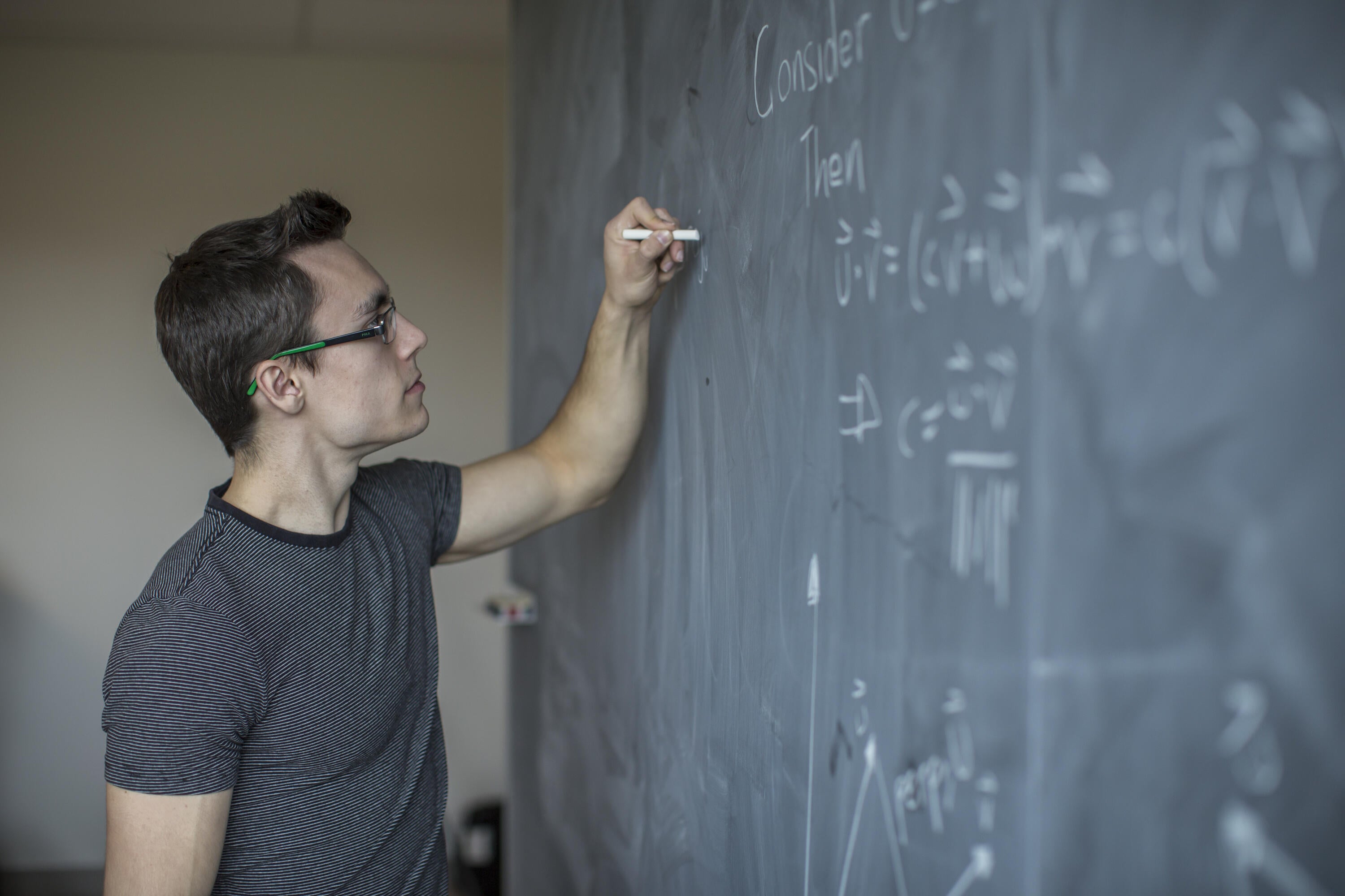 A students using chalk to write out math equations on a chalkboard.