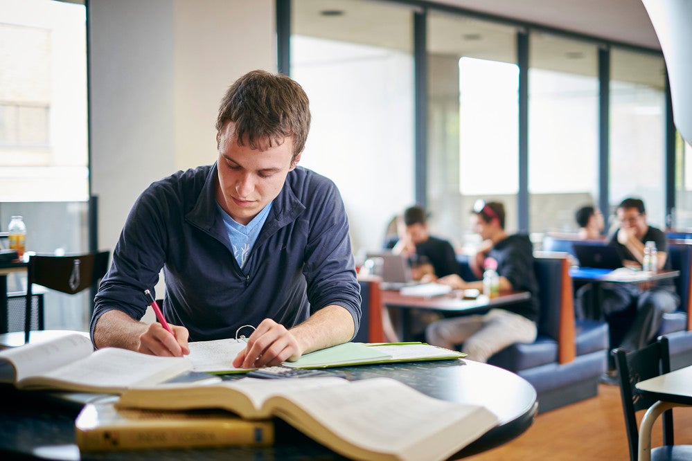 A student sitting at a desk with textbooks open as they write notes.