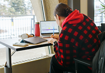 A student studying at a desk by a window on campus