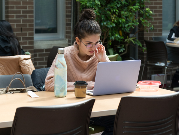 A student sitting at a table with a laptop, water bottle and coffee.