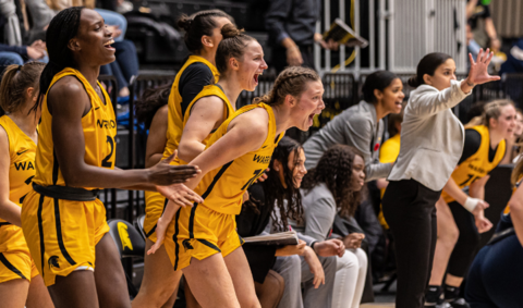 Women's Warrior basketball team cheering from the sidelines of the basketball court