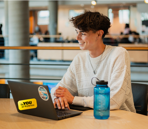 Student sitting at a laptop with a Be You sticker on it