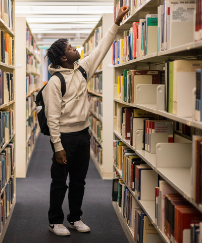 Student reaching for a book on the library shelves