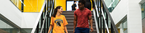Two students walking down a set of stairs in athletic gear inside the PAC.