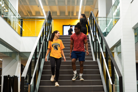 Two students walking down a set of stairs in athletic gear inside the PAC.
