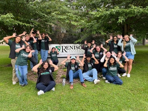 A group of students making a mouse antler sign in front of the Renison sign.