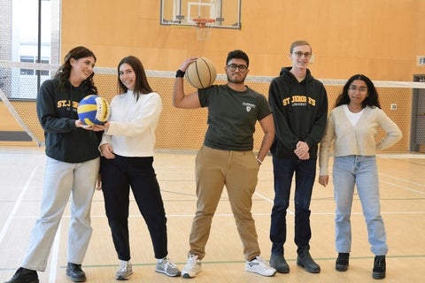 A group of 5 students on the St. Jerome's indoor activity court, in front of the volley ball net.