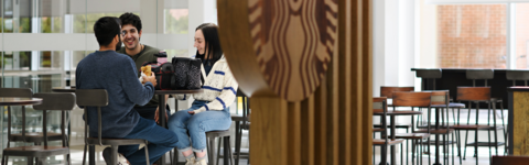three students sitting at a table chatting and smiling