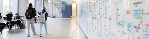 Students walk down a long hallway with a whiteboard wall