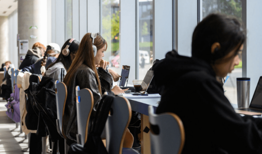 Students sitting along a window with heads down studying