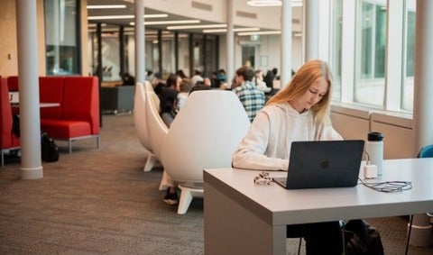 Student sitting at table with laptop, taking notes