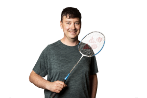 student standing smiling and holding a badminton raquet
