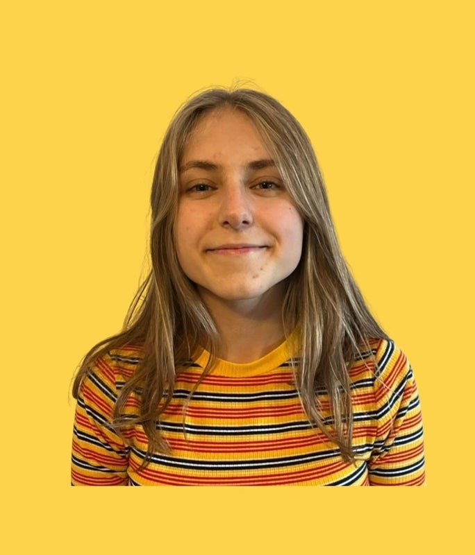A girl smiling at the camera, wearing a black, yellow, and orange top.
